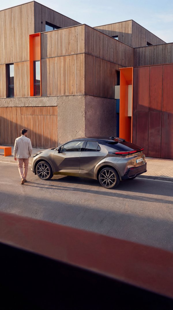 AI photoshoot: man in beige blazer walking away from Toyota C-HR modern architecture
