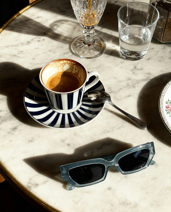 AI product photography: blue-gray sunglasses on marble cafe table with espresso